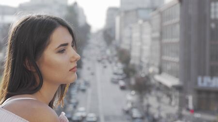 Sad woman looking away at blurry city streets. Unhappy young woman observing busy city center. Depressed woman looking away thoughtfully. Depression, loneliness conceptの写真素材