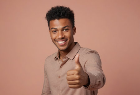 A young adult male with a bright smile gives a thumbs up to the camera. Hes wearing a casual button-up shirt with a coral background.の素材