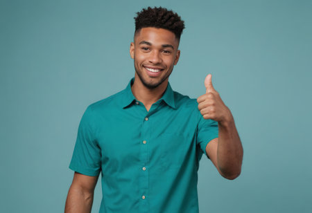 A young man in a teal collared shirt gives a thumbs up, his confident smile radiates against a teal backdrop.の素材