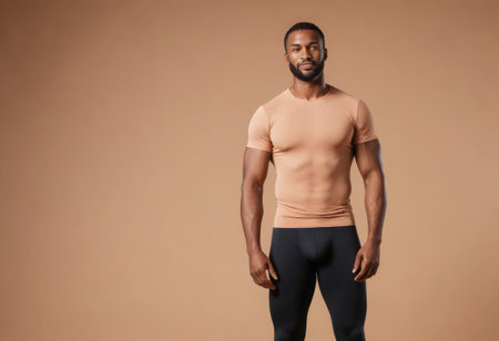 A strong man stands confidently in a fitted peach shirt, his athletic build apparent.の素材