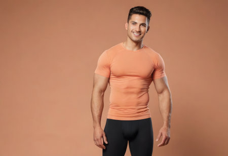 A fit man stands in a peach t-shirt, showing off a toned physique. His posture and attire highlight a balance of style and fitness.の素材