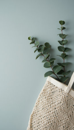 A stylish, woven tote bag rests against a soft, muted blue wall, adorned with vibrant green eucalyptus sprigs peeking out. This serene composition evokes a sense of calm and connection to nature, blending modern aesthetics with organic beauty.の素材