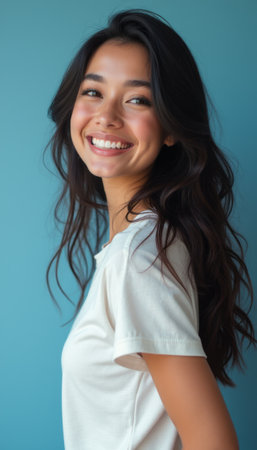 A joyful young woman with long, flowing hair beams with happiness, showcasing her bright smile against a calming blue background. Her warm expression radiates positivity and confidence, inviting viewers to share in her uplifting energy.の素材