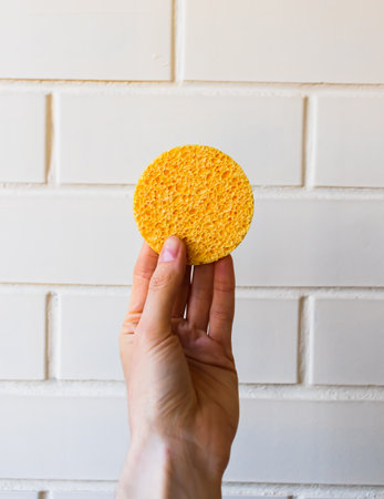 female hand holding reusable pad for washing face on white background. Cleansing skin care accessory. make-up removal concept.の写真素材
