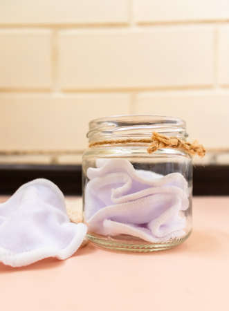 Zero waste lifestyle. Reusable organic cotton pad for make-up remover and facial cleansing, knitted eco bag, storage jar on pink background. Eco-friendly beauty accessory.の写真素材