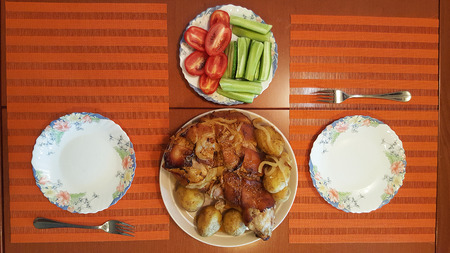 roasted pork knuckle with potatoes, tomatoes and cucumbers on a plate for twoの写真素材