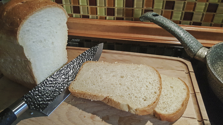 sliced bread on an old wooden board with a black knifeの写真素材