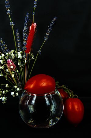 art photo tomato on a glass of water with a bouquet of flowers on a black backgroundの写真素材