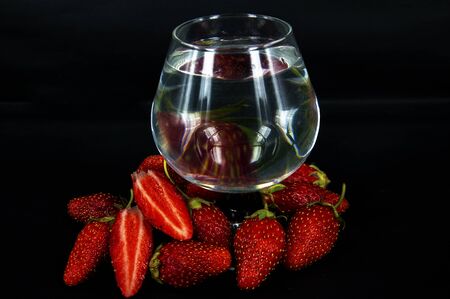 photo whole and sliced strawberries closeup with a glass of water on a black backgroundの写真素材