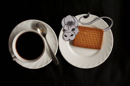 photo still life of a cup of coffee with a rectangular cookie and a painted bull on a black backgroundの写真素材