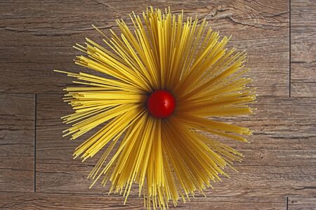 photo of spaghetti in the form of a flower on a wooden background with a tomato in the centerの写真素材