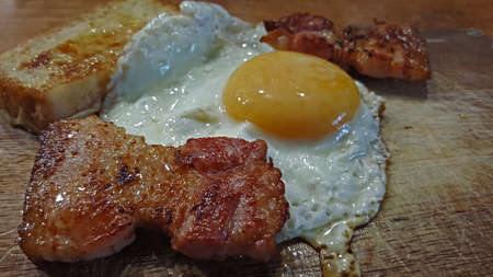 photo close-up side view of fried eggs with pieces of fried bacon and croutonsの写真素材