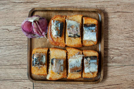 photo of grated garlic croutons with fish pieces on a square wooden plate