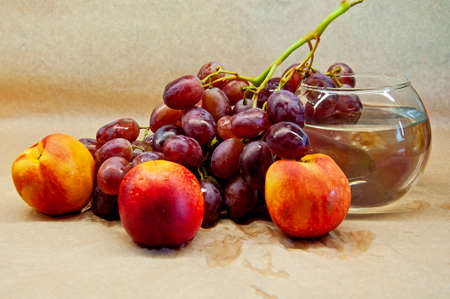 photo of a brush of grapes with nectarine with a glass on a beige backgroundの写真素材