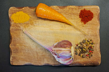 photo of pepper, turmeric, garlic, paprika on a wooden board on a dark backgroundの写真素材