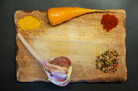 photo of pepper, turmeric, garlic, paprika on a wooden board on a dark backgroundの写真素材