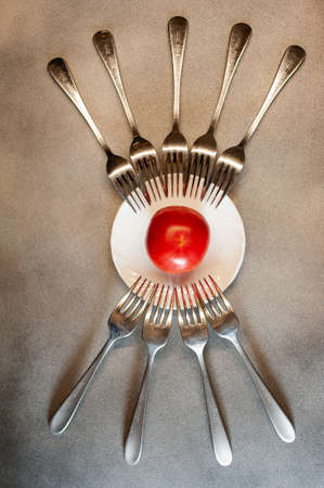forks around a plate like eye and eyelashes close-up on a gray background with tomato colorの写真素材