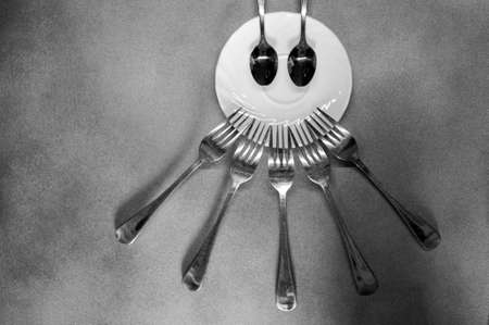 photo of forks and spoons around a plate like a face close-up on a gray backgroundの写真素材