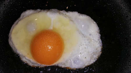 photo of fried eggs from one egg on a black frying pan close-upの写真素材