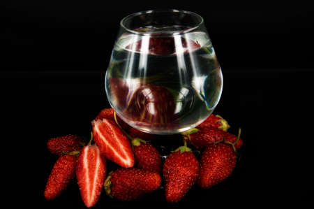 art photo whole and sliced strawberries closeup with a glass of water on a black backgroundの写真素材