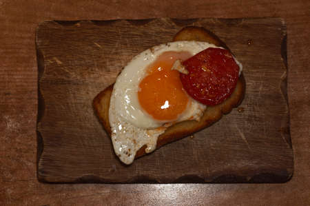 art photo of fried eggs with tomato slices fried in butter on toast and a wooden boardの写真素材