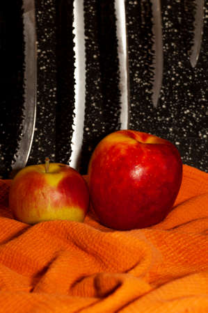 art photo of two ripe apples on an orange napkin against the background of knivesの写真素材