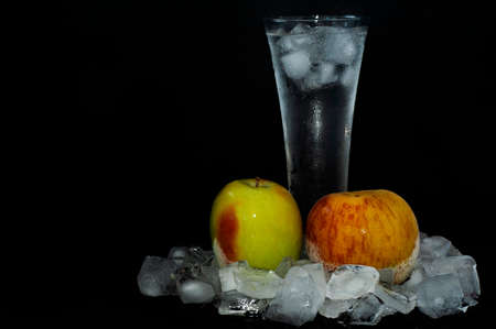 glass with ice thawing frozen apples among ice cubes close-up on a black backgroundの写真素材