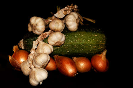 horizontal photo of zucchini and heads of onions and garlic close-up on black backgroundの写真素材