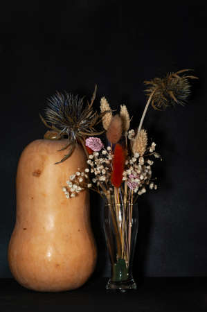 vertical art photo of a pear-shaped pumpkin and a bouquet of dried flowers close-up on a black backgroundの写真素材