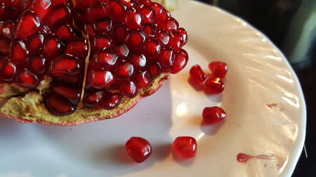 photo of a cut pomegranate on a plate with dropped seeds close-upの写真素材