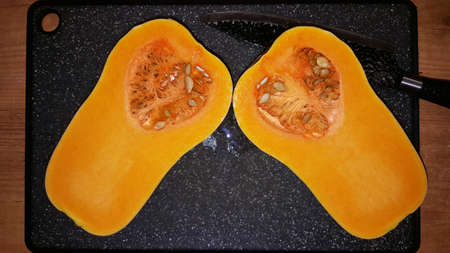 art photo of a cut pear-shaped pumpkin with seeds on a black boardの写真素材