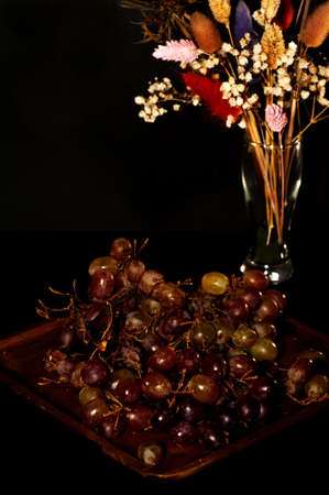 art photo of grapes on a wooden plate with a bouquet of dried flowersの写真素材