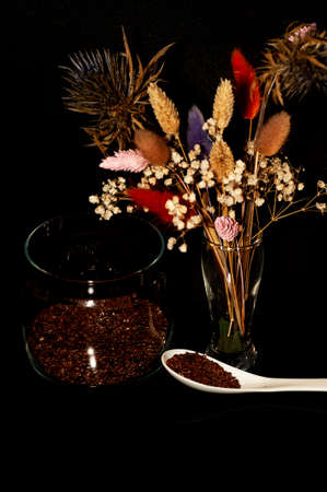 art photo of flax seeds in a jar and a spoon with a bouquet of dried flowers on a black backgroundの写真素材