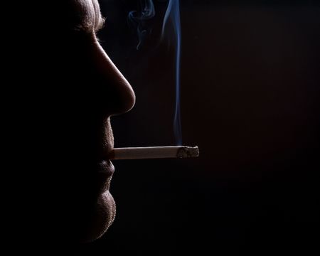 The man smokes a cigarette against a dark backgroundの写真素材