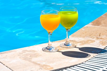 Two glasses with juice on the brink of poolの写真素材