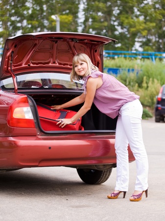 young woman puts the suitcase in the trunk of a carの写真素材