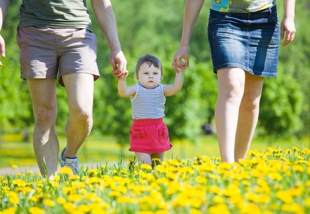 Family on walk in park. Parents go on park and hold the little girl for hands.の写真素材