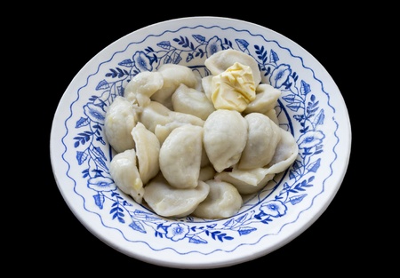 The blue patterned plate full of dumplings, seasoned with a piece of butter. Isolated on a black background.の写真素材