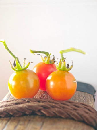 Three fresh cherry tomatoes with stems placed together on a rustic wooden surface, symbolizing natural and organic food.の写真素材