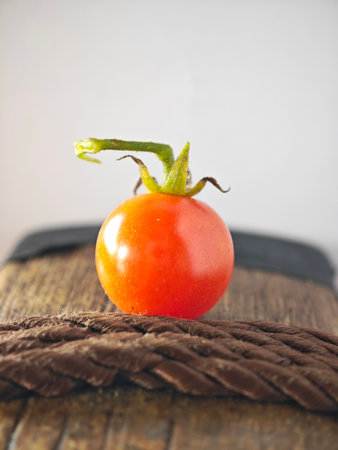Close-up of a single ripe cherry tomato placed on a rustic wooden surface with natural lighting.の写真素材