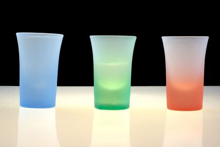 Three vodka glasses of different colors on black background, illuminated from belowの写真素材