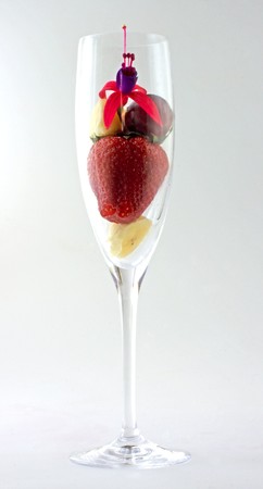 Fruit salad with strawberry, banana, grape, cheese and a flower all in an elegant white wine glassの写真素材
