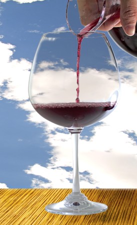 Male hand pouring red wine from a decanter to a big glass, blue cloudy sky on the backgroundの写真素材