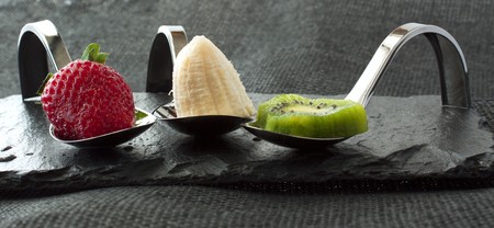 Strawberry, banana and kiwi over elegant restaurant metal spoonsの写真素材