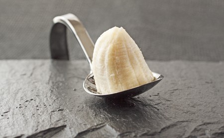 Slice of banana on a metal spoon, over black backgroundの写真素材
