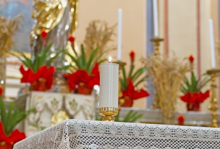 Candle lit on an altar with flowers on the backのeditorial素材