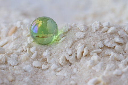 Green glass marble over a background of white sand