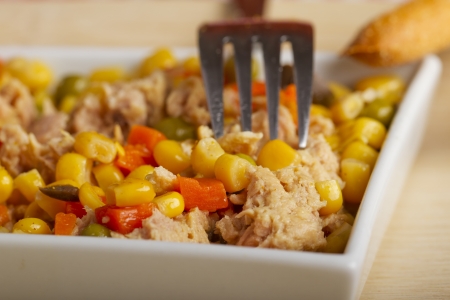 A salad with corn, carrots and tuna in a white square plateの写真素材