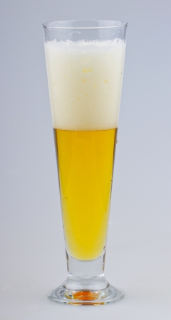 A glass of beer with foam over gray backgroundの写真素材