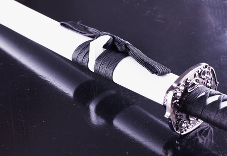 Katana in white case, over black reflecting background, horizontal image